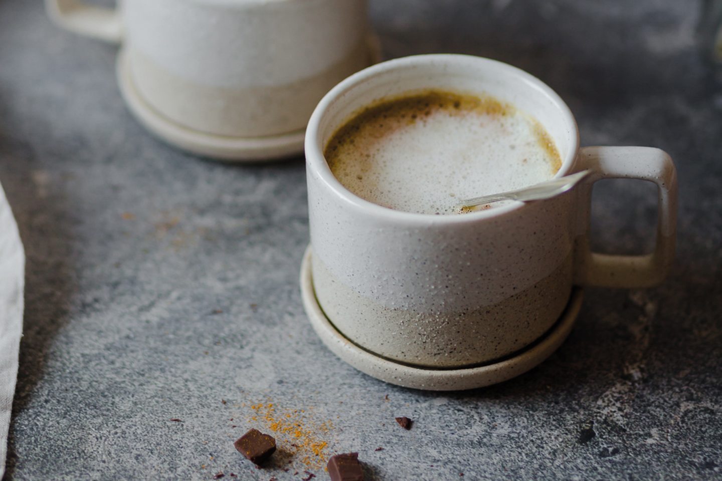 Tasse mit heißer Curcuma-Schokolade und etwas Schokolade auf grauem Untergrund