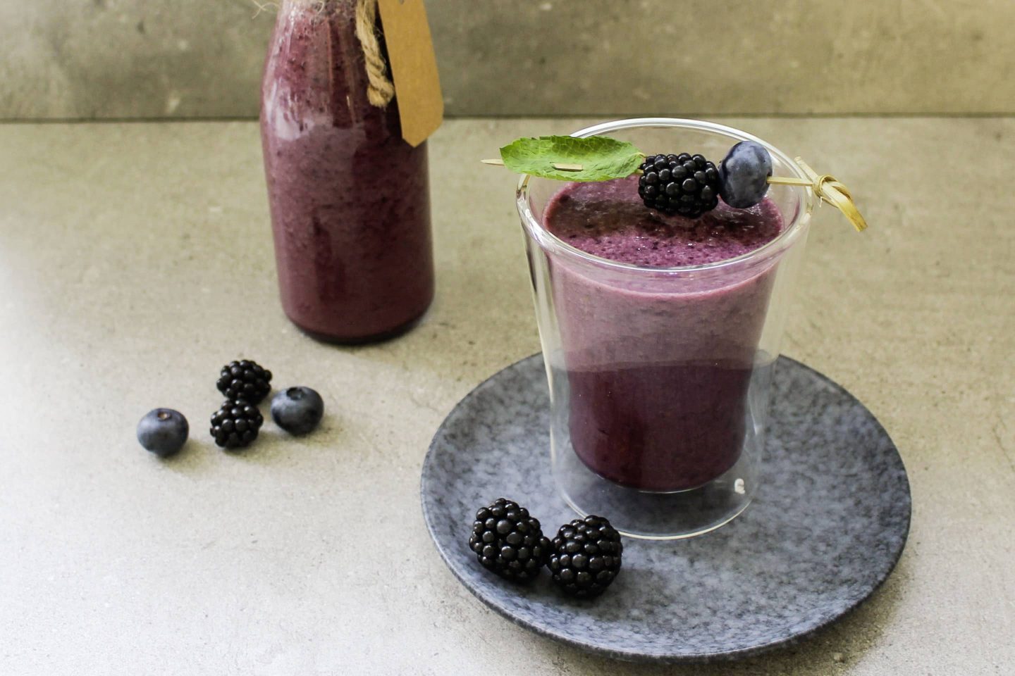 Brombeer-Bananen-Shake mit Veggy Sweet in einem Glas und einer Flasche mit frischen Beeren garniert