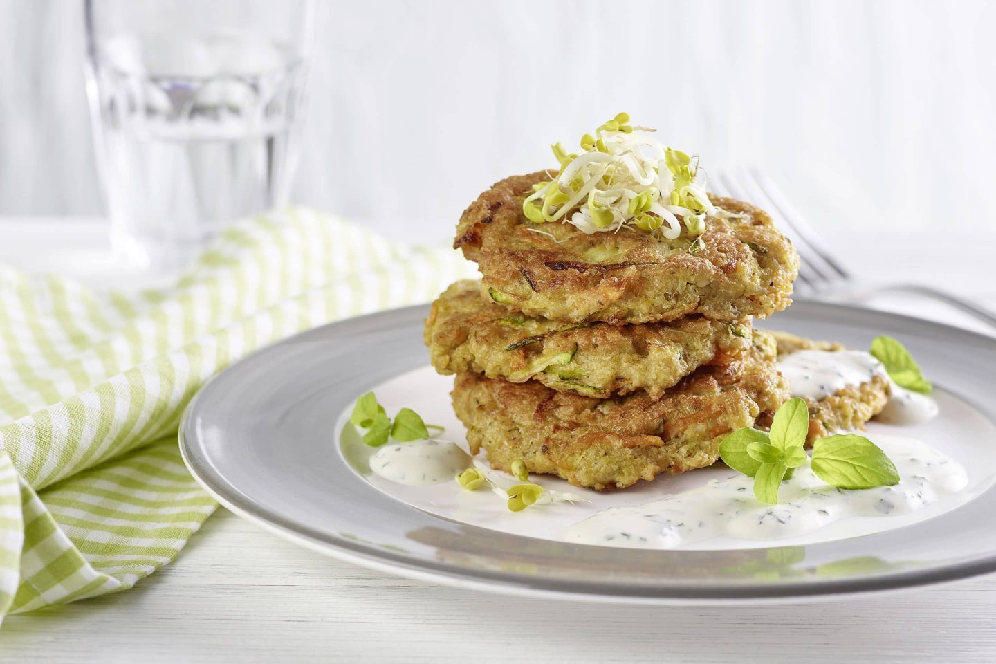 Karotten-Zucchinilaibchen mit Haferflocken und Majoran zubereitet auf einem Teller mit grauem Rand und grün-karierter Serviette