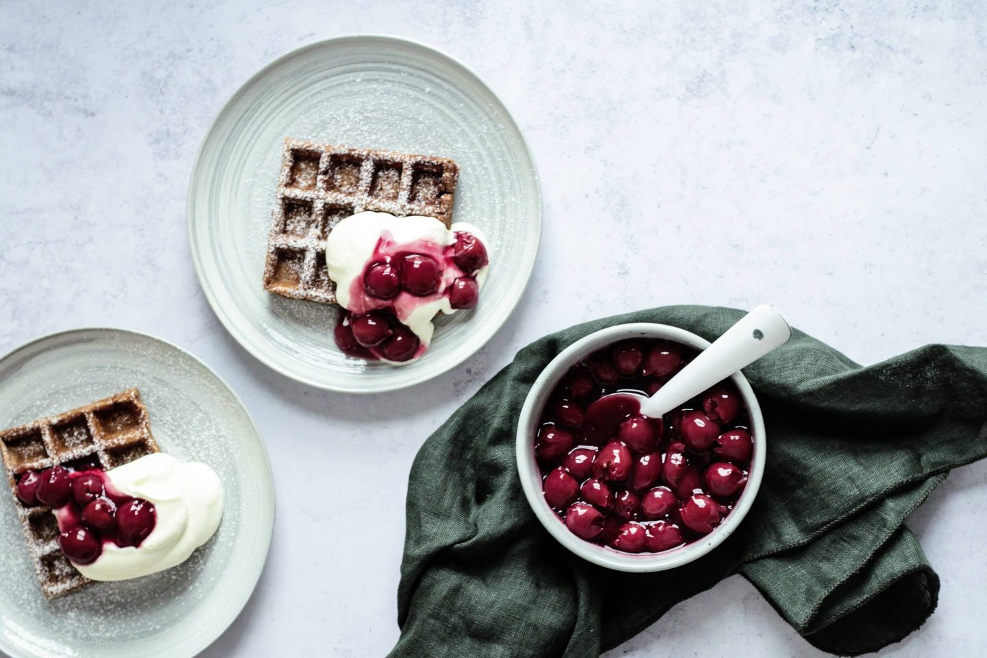 Waffeln mit Lebkuchengewürz und Glühweinkirschen auf mint-farbenen Tellern mit Schlagobers und Puderzucker