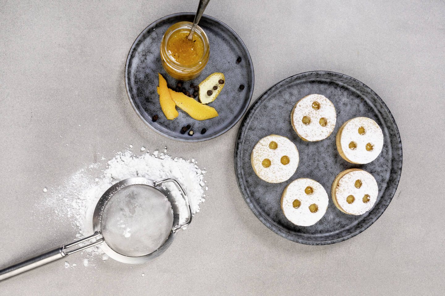 Linzer Augen mit Pfeffer-Orangenmamelade auf einem blauen Teller mit Staubzucker bestreut