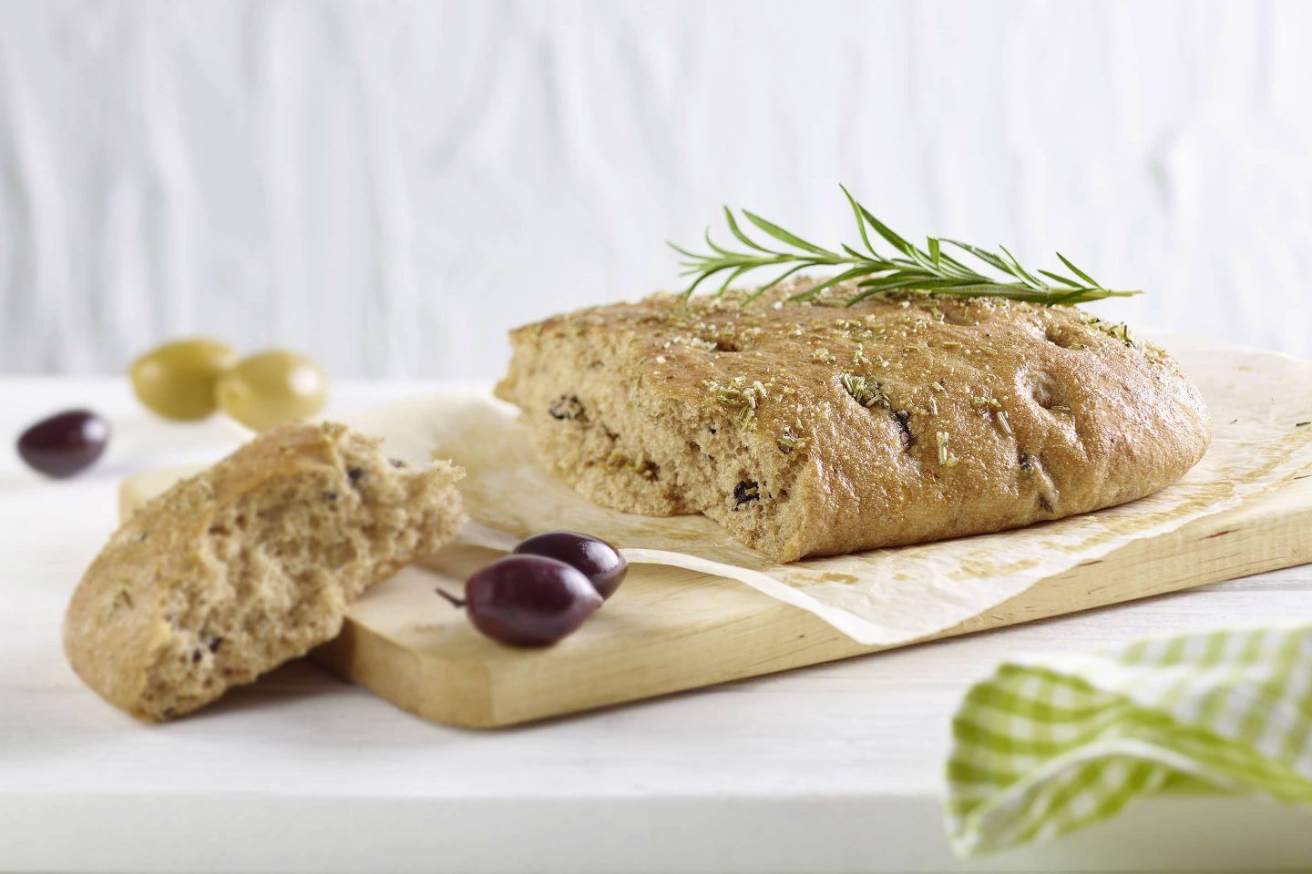 Vollkorn Foccacia mit Rosmarinzweig und Oliven auf einem Holzbrett
