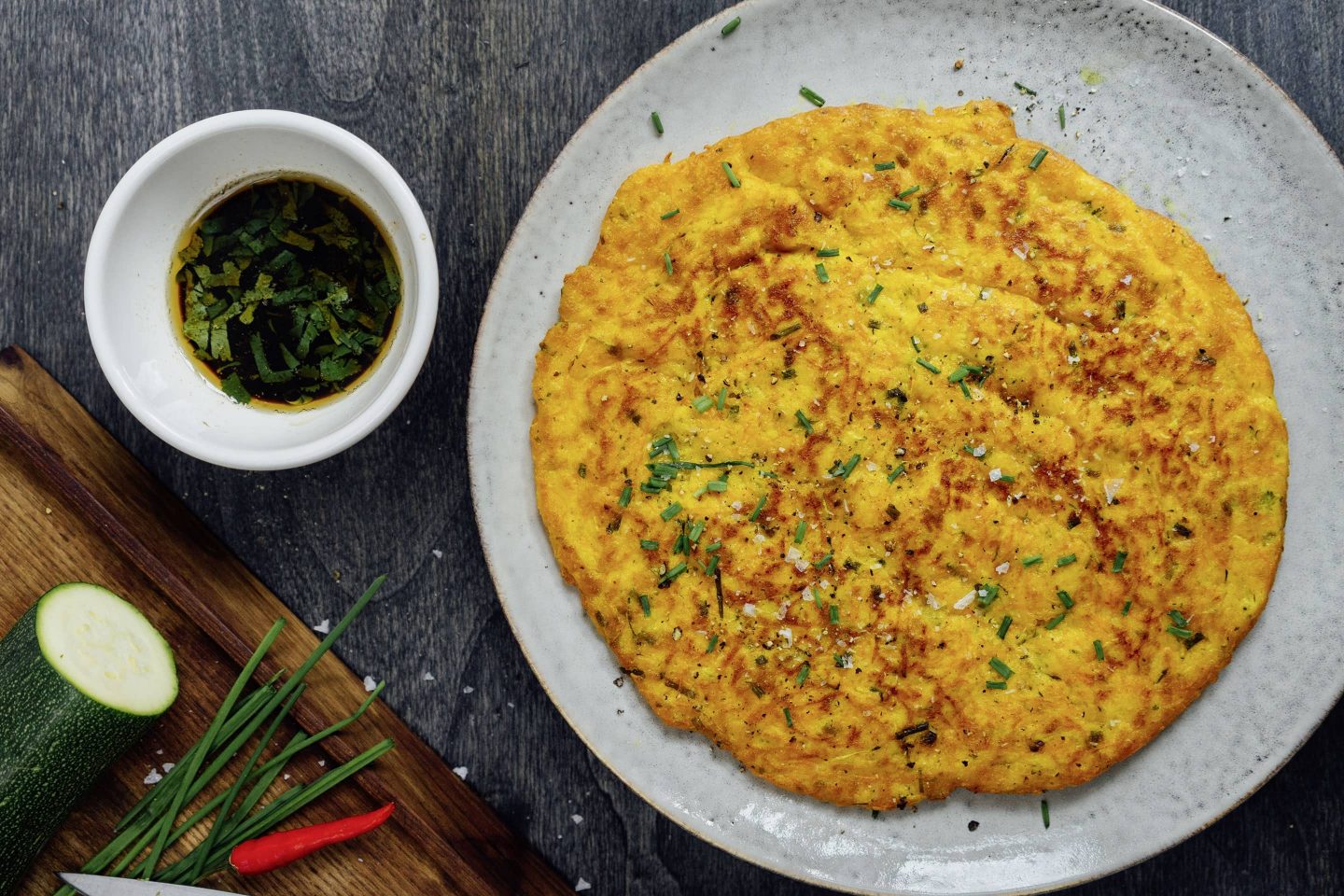 Zucchini-Curry-Schmarrn auf einem hellen Teller mit einem Schälchen voll Sojasauce