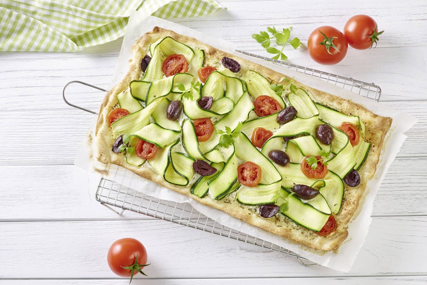 Zucchini-Flammkuchen mit Liebstöckel frischen Tomatenscheiben und schwarzen Oliven auf einem Gitter