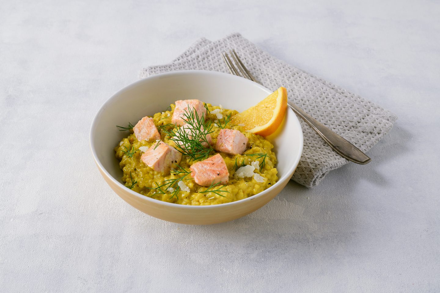 Orangen-Lachs-Risotto mit Curcuma & more Karotte verfeinert und frischem Dill und Orangenspalte in einer Schale angerichtet