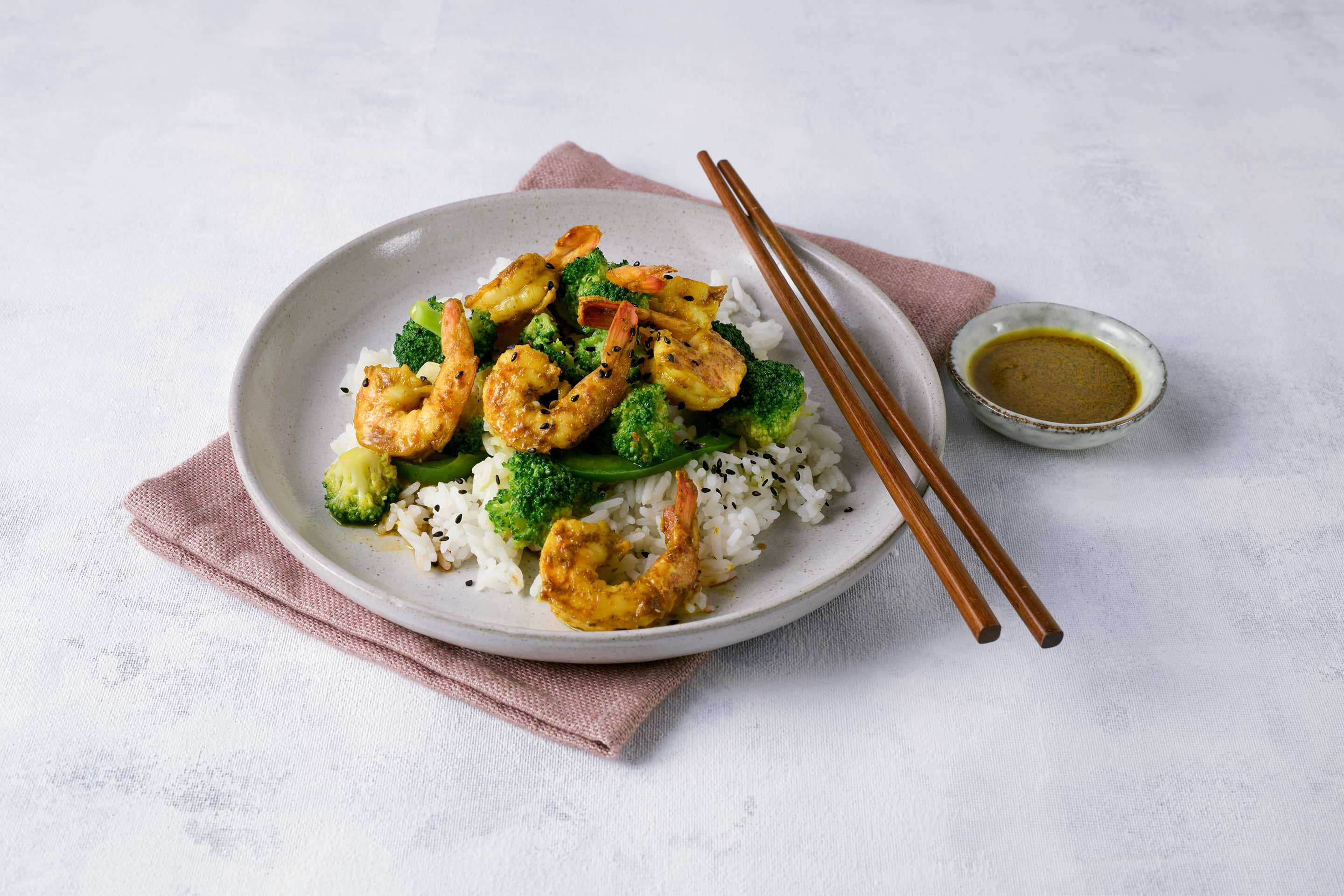 Garnelen mit Brokkoli im Wok zubereitet mit Curcuma & more auf einem hellen Teller mit Essstäbchen angerichtet