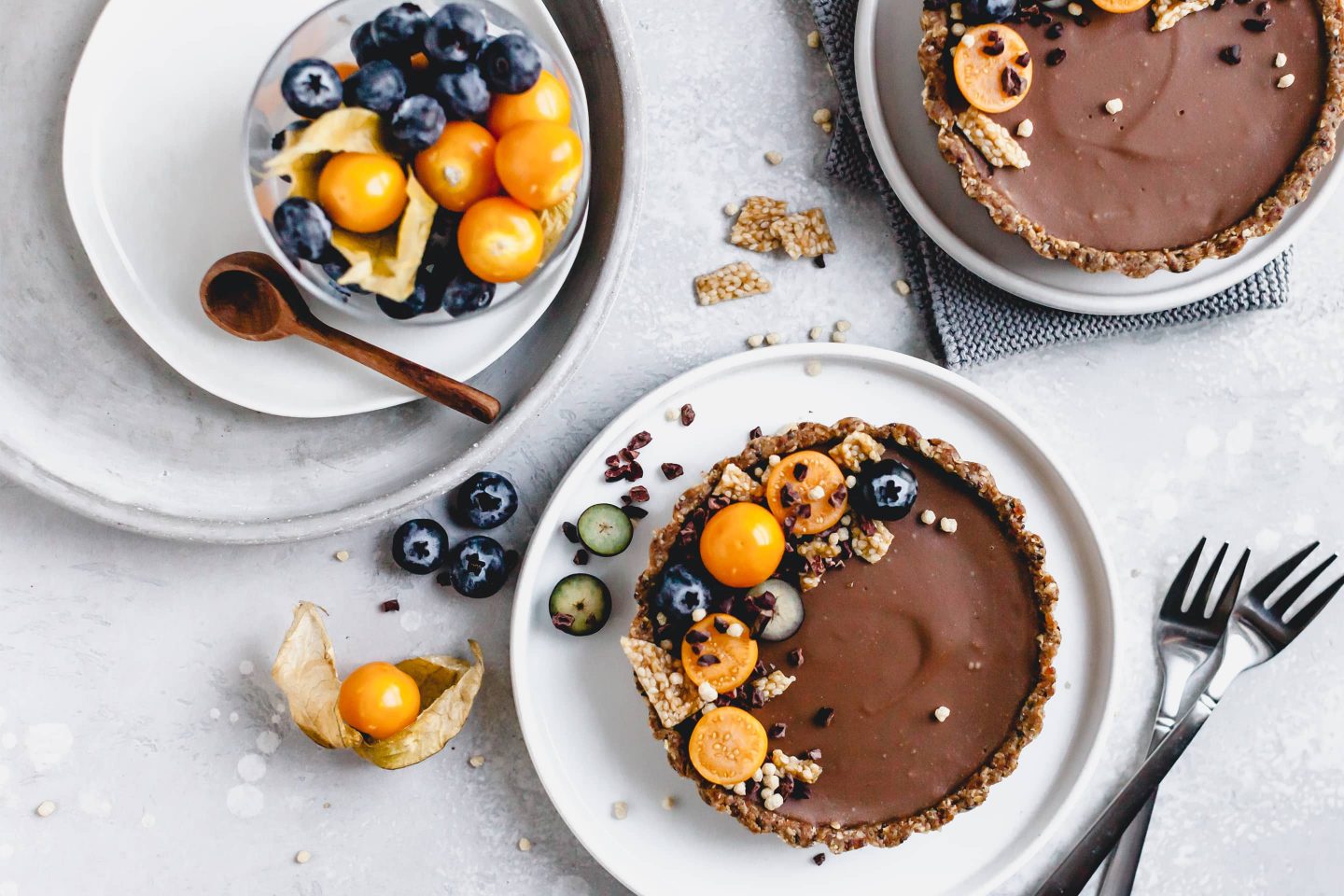 Schoko Tartelettes mit frischen Physalis und Blaubeeren dekoriert und auf Tellern angerichtet