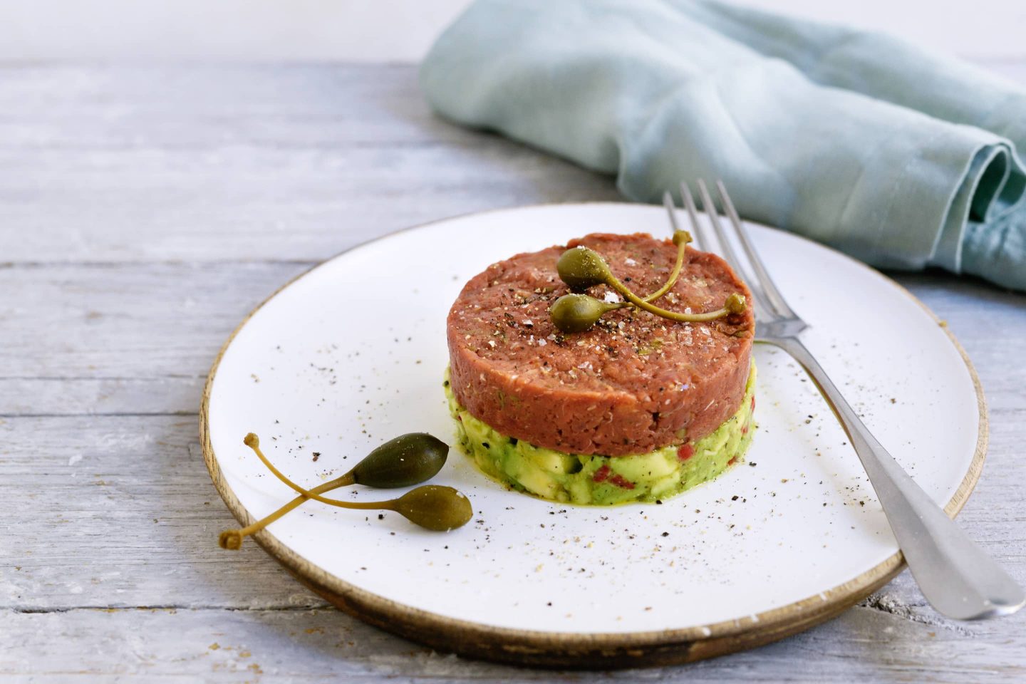 Beef & Avocado Tartar mit Bio Oregano mit ein paar Kapern auf einem hellen Teller angerichtet