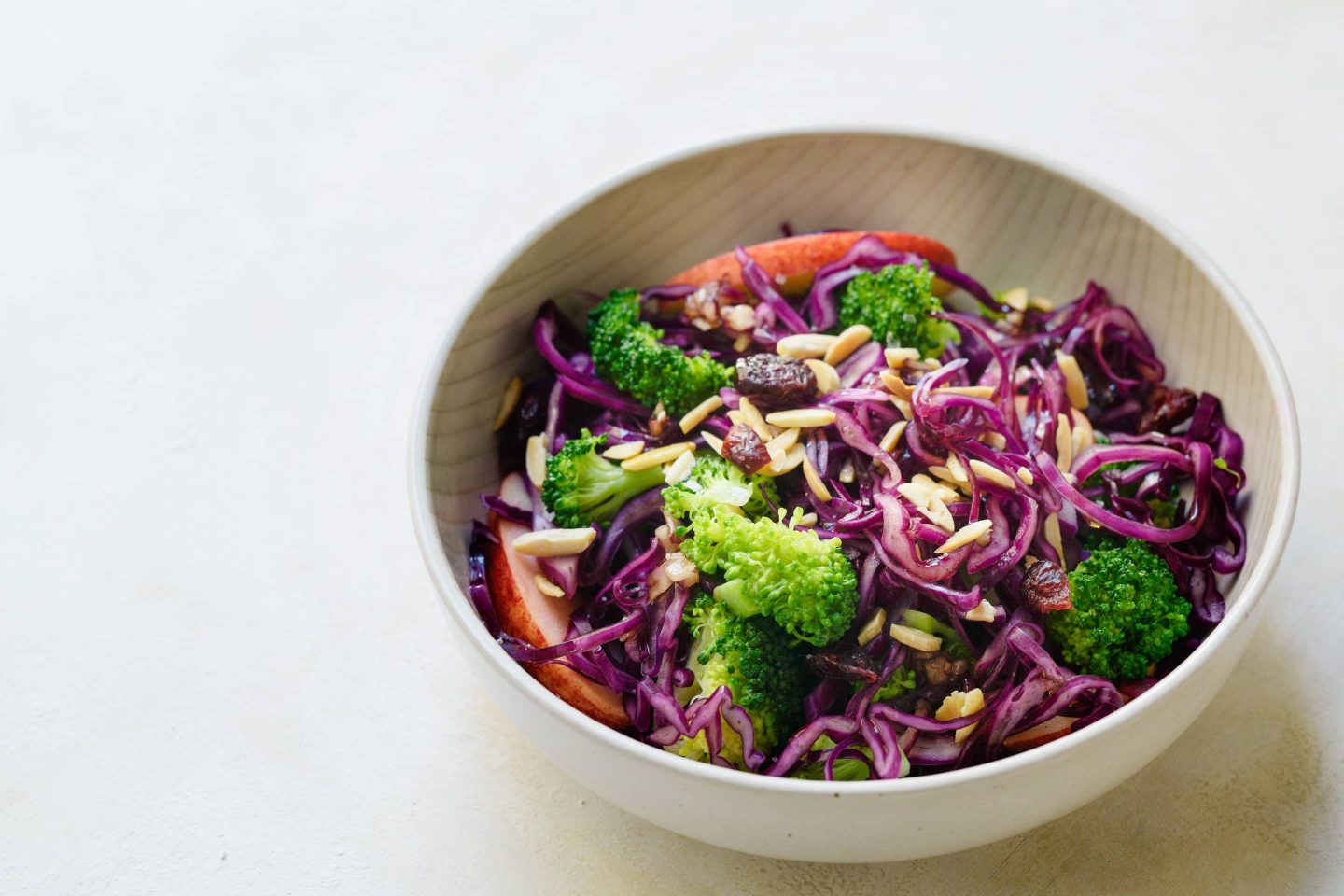 Winterlicher Brokkoli-Rotkraut Salat mit Rosmarin, Äpfeln und Mandeln in einer cremefarbenen Schüssel