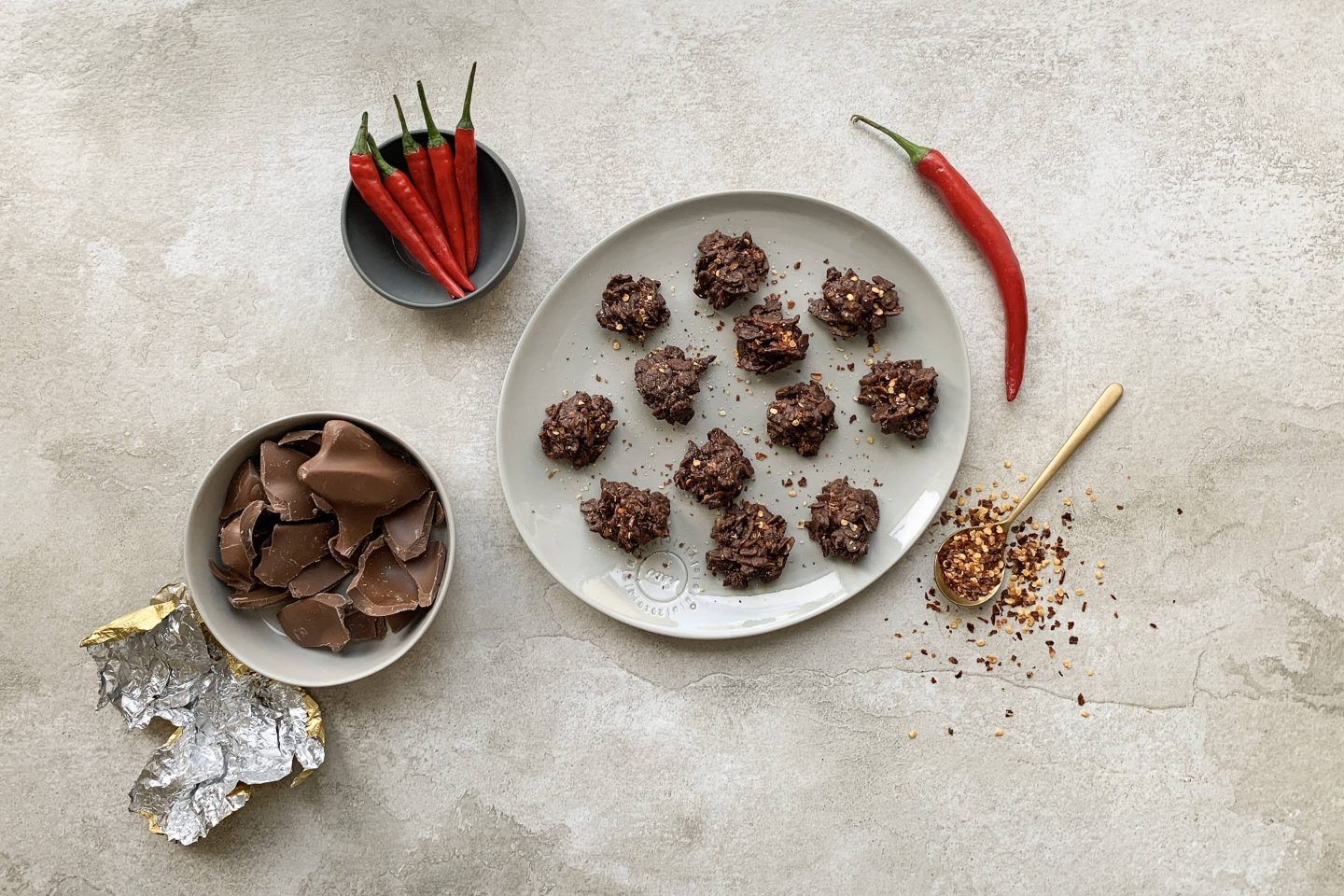 Schoko Crispies mit Meersalz und Chili auf einem grauen Teller mit Chilischoten und etwas Schokolade angerichtet