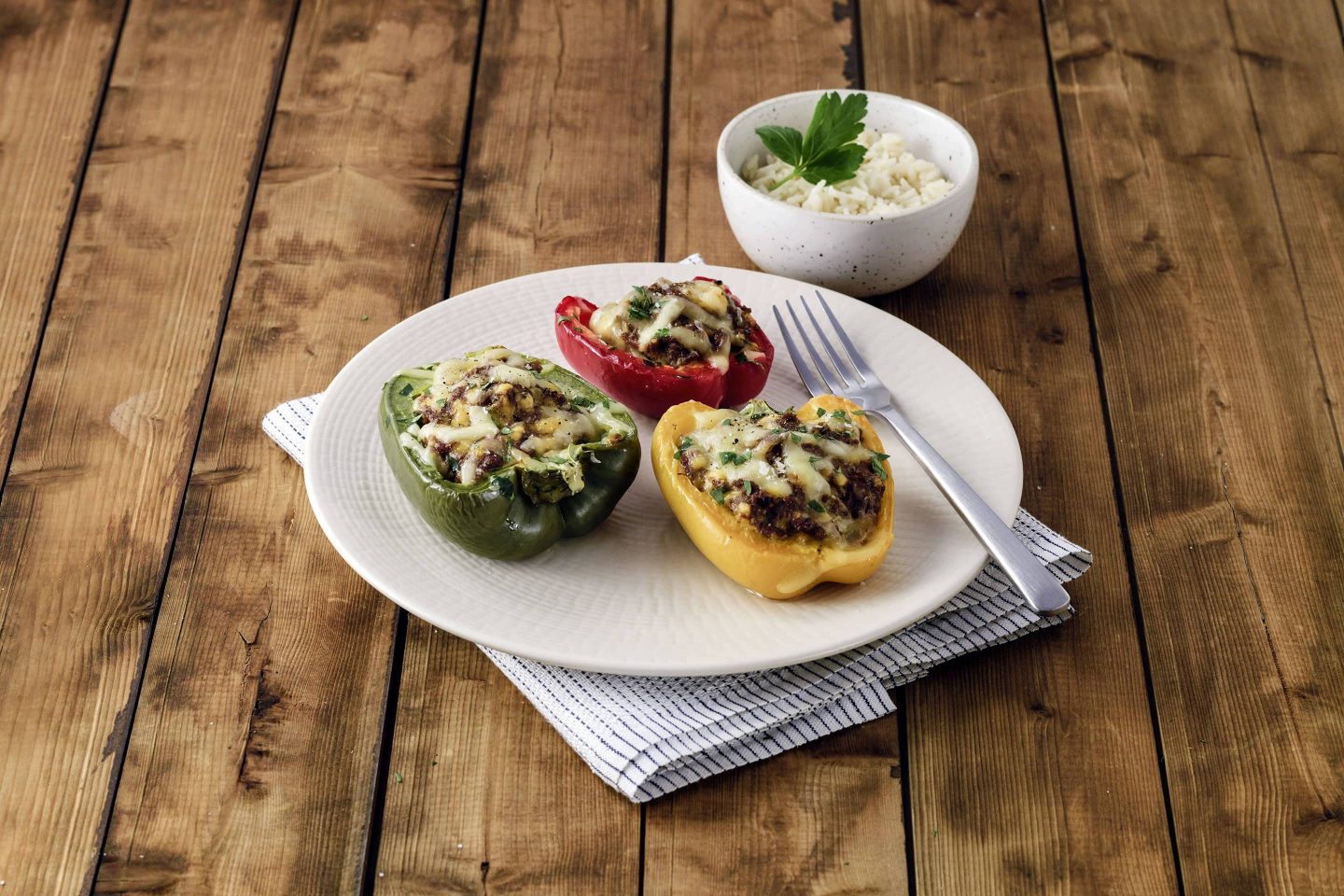 3 halbe gefüllte Grill-Paprika mit etwas geschmolzenem Käse und einer Schüssel Reis