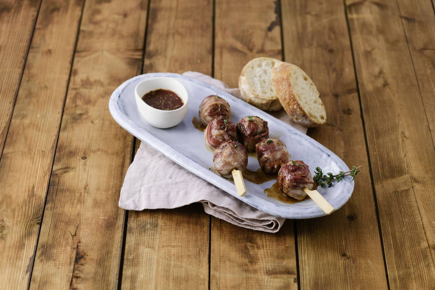 Grill-BBQ-Meatballs auf Spießchen mit Sauce und etwas Baguette auf einem ovalen Teller
