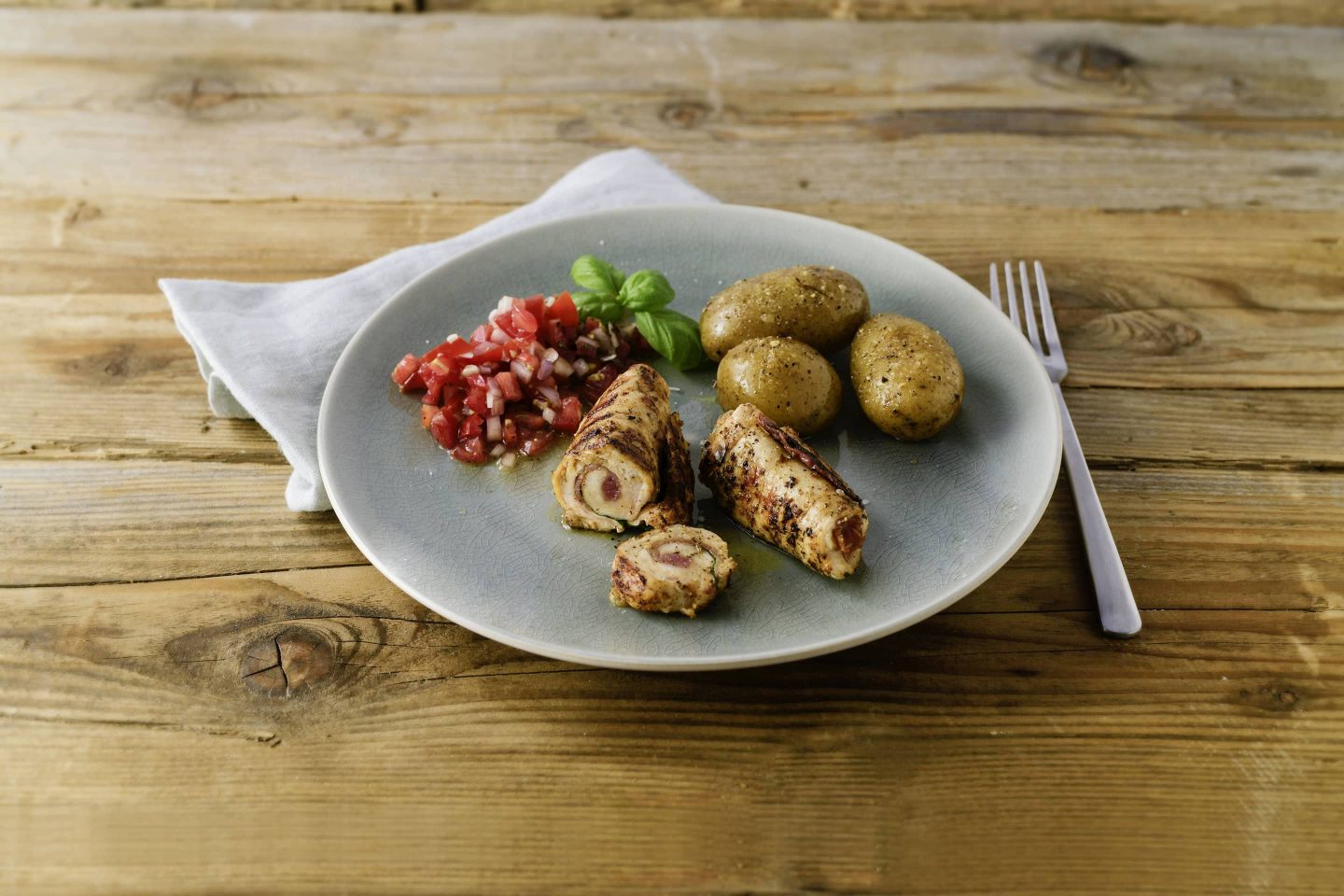 Grill-Gefluegel Involtini mit Kartoffeln und Tomatensalsa auf einem hellgrauen Teller