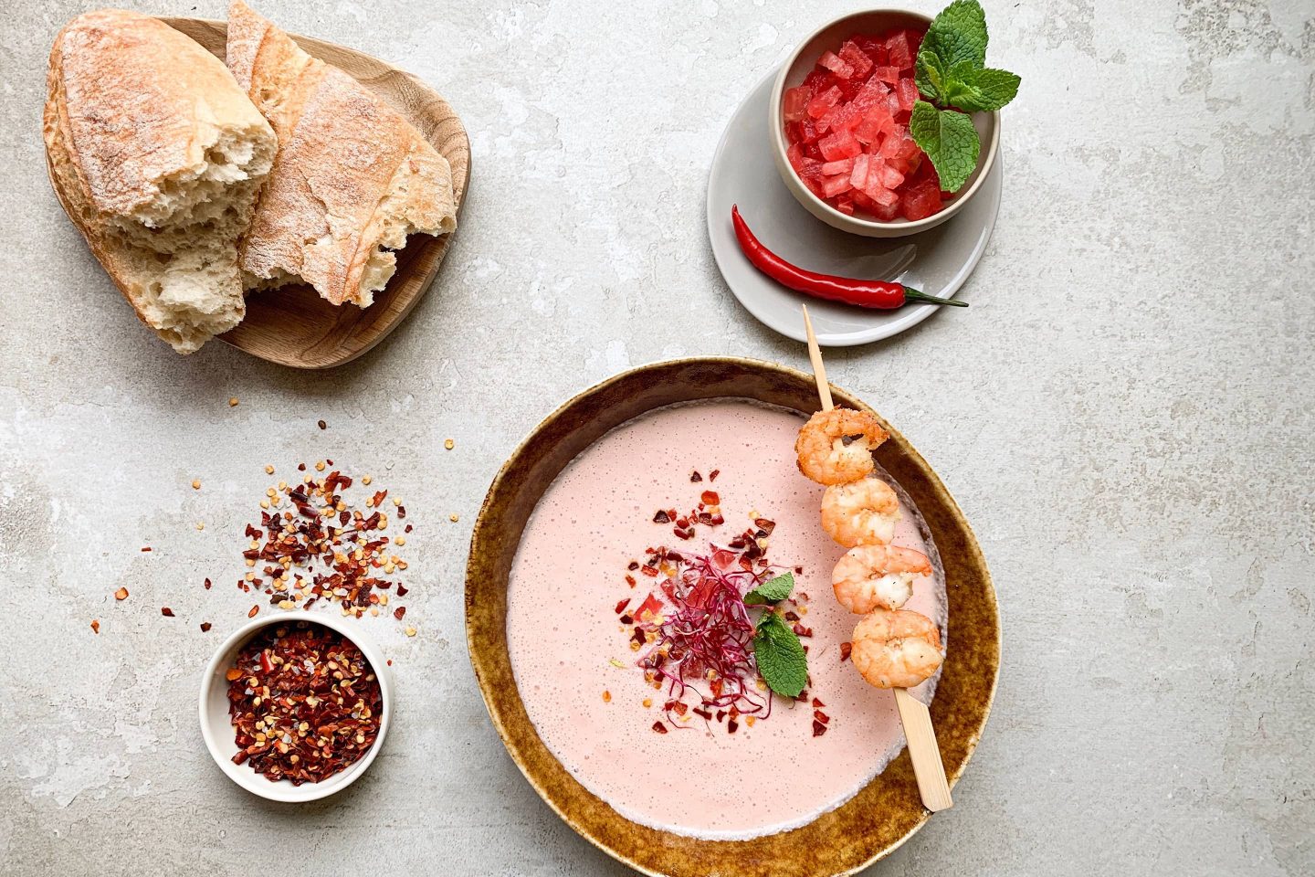 erfrischende Wassermelonensuppe mit Chili und einem Garnelenspieß in einer braunen Schale mit Weißbrot
