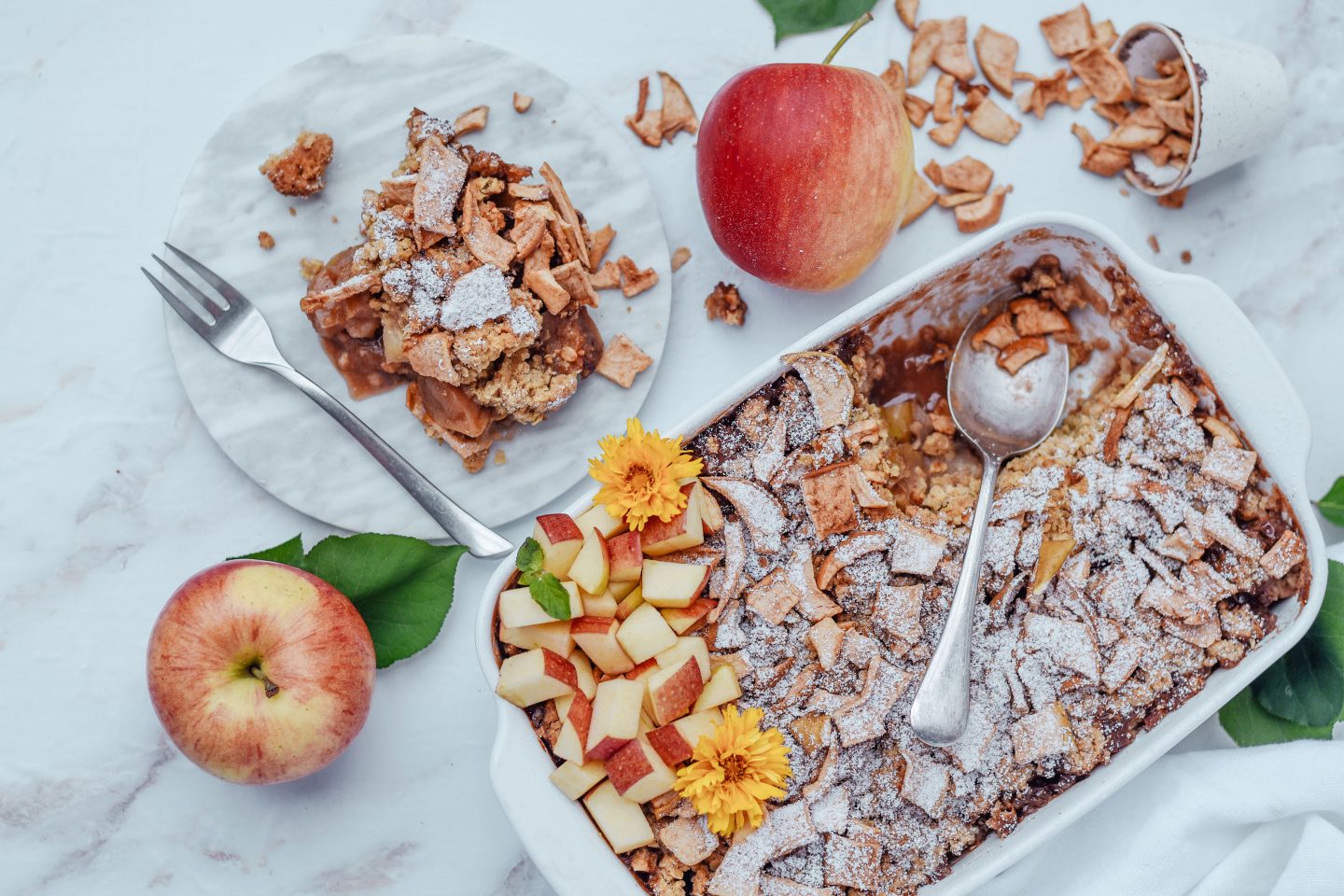 Apfel-Crumble mit Apfel-Zimt- Chips in einer Auflaufform und Äpfeln