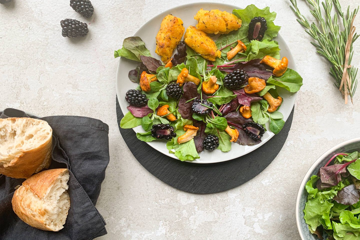 Eierschwammerl Salat mit Brombeeren und Brot auf einem hellgrauen Teller angerichtet