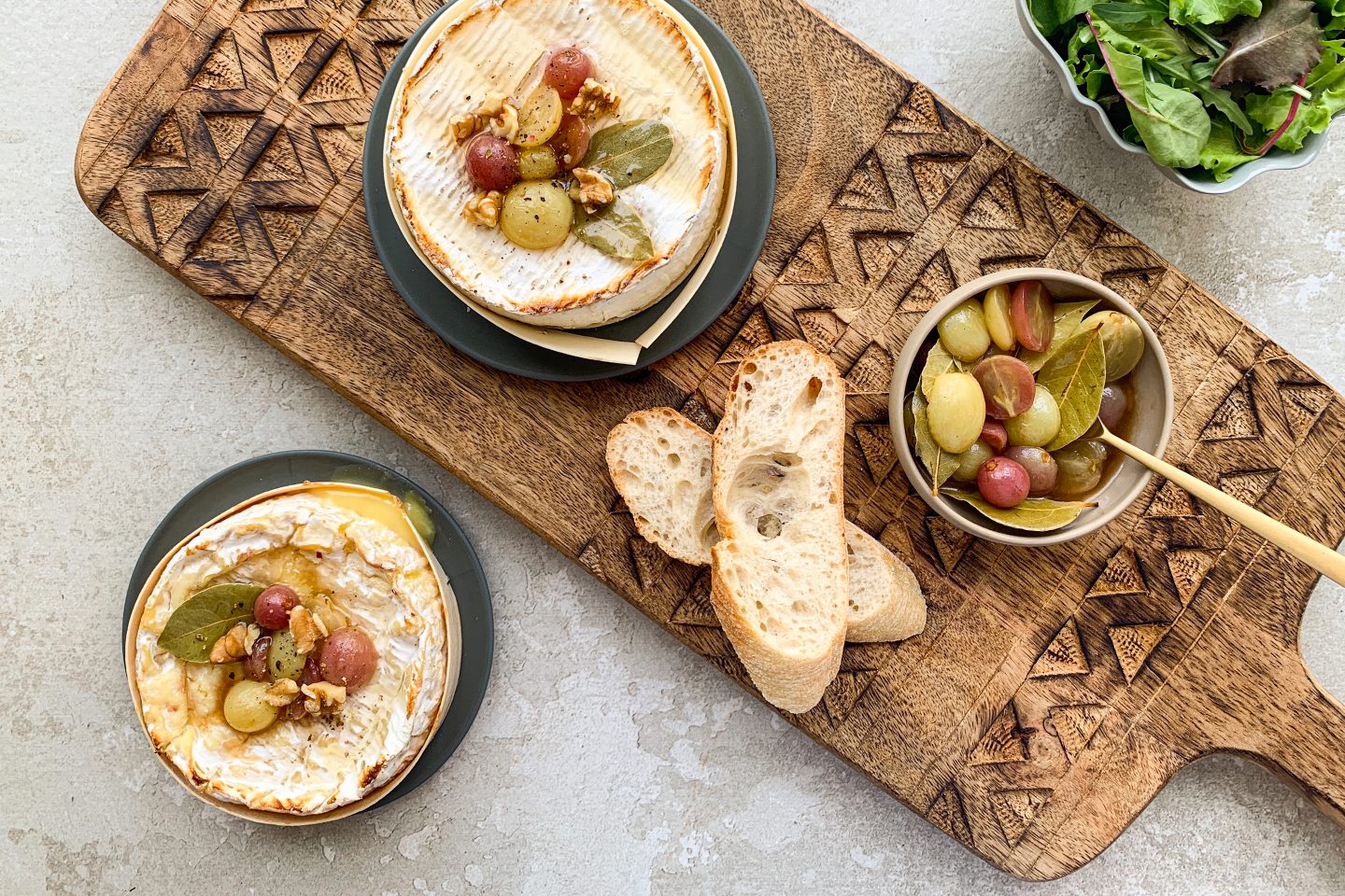 Glasierte Weintrauben auf gebackenem Camembert mit Baguette und Salat auf einem Holzbrett angerichtet