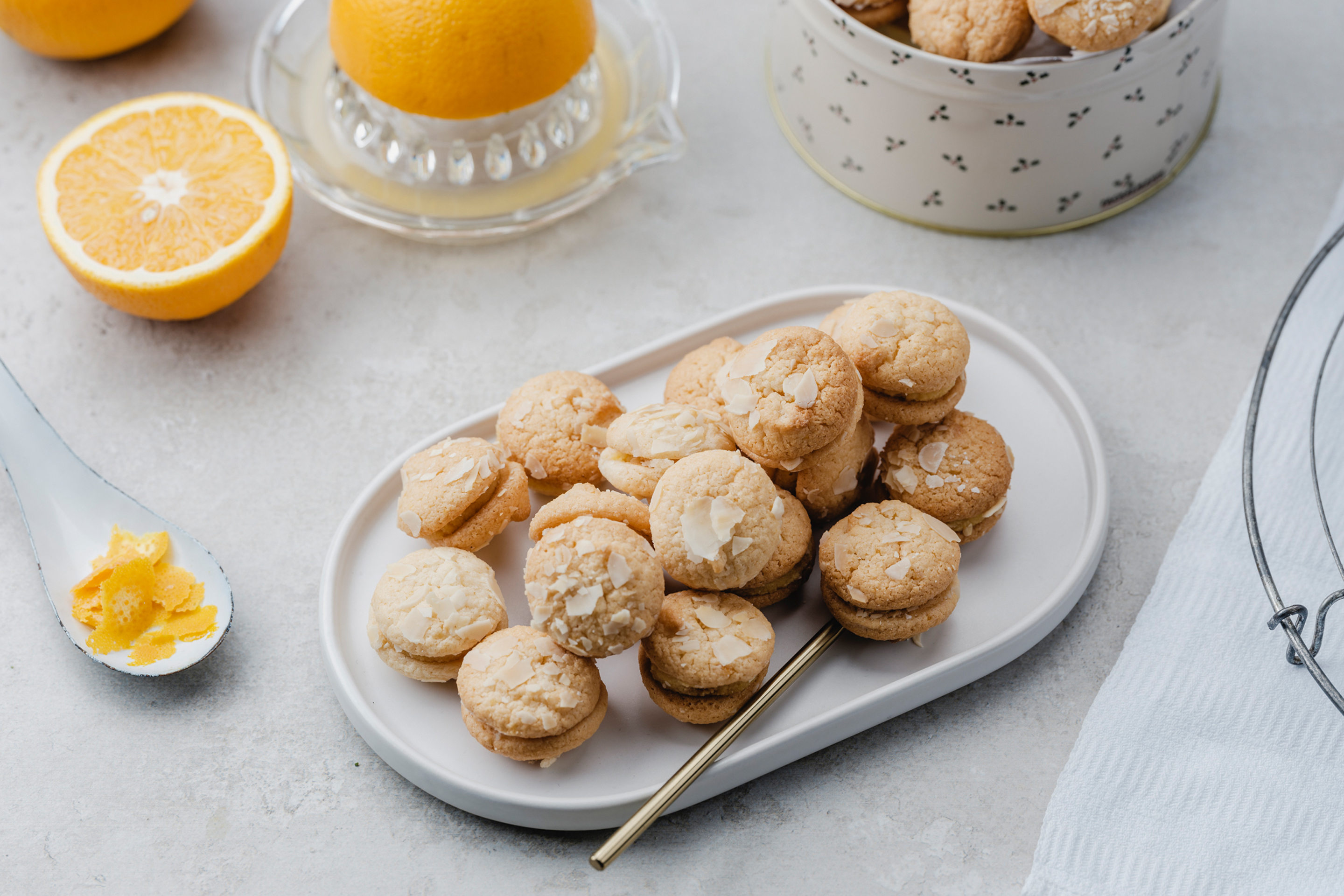 Orangenkekse mit Marzipan auf einem ovalen Teller mit Ornagenhälften und -zeste