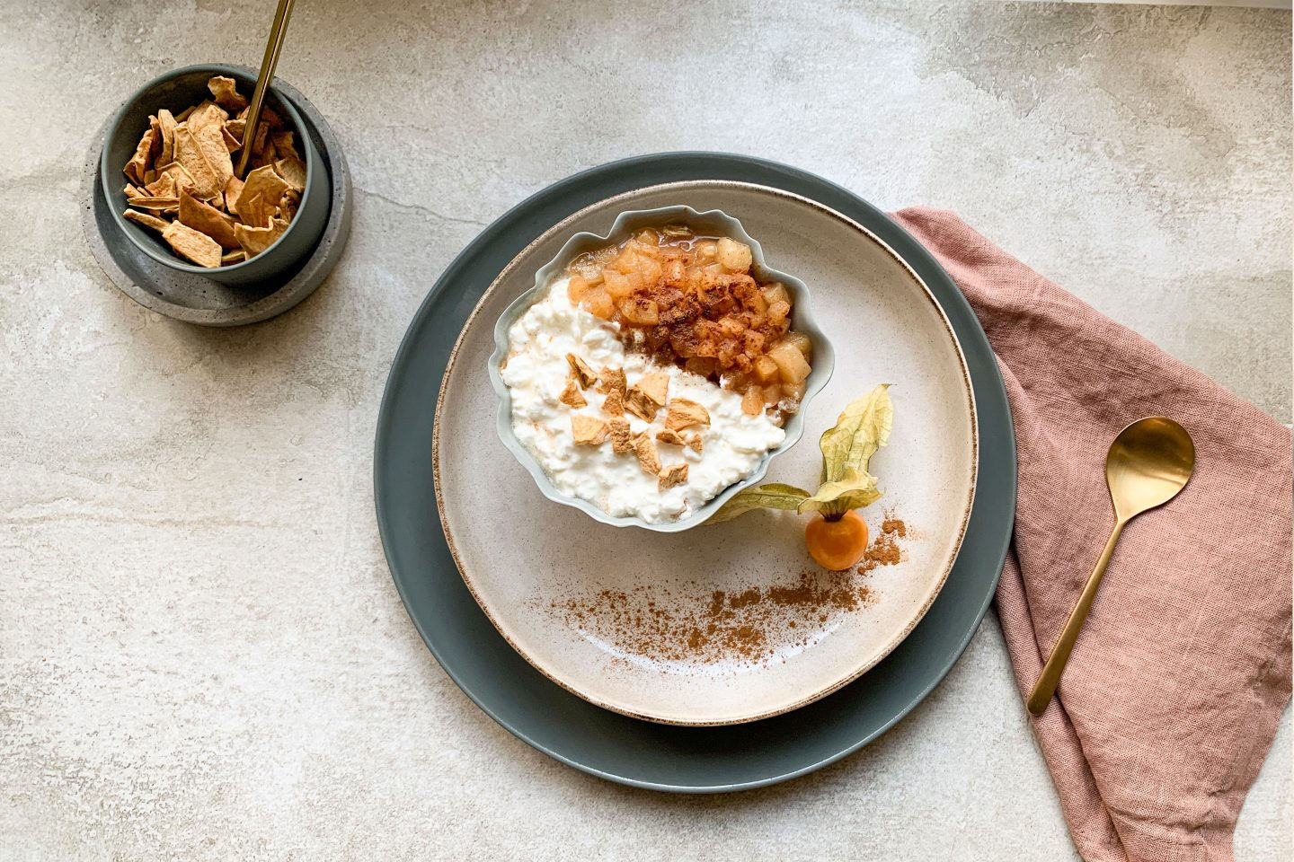 Hüttenkäse mit Apfel und crunchy Topping in einer Schale auf einem Teller mit Physalis angerichtet
