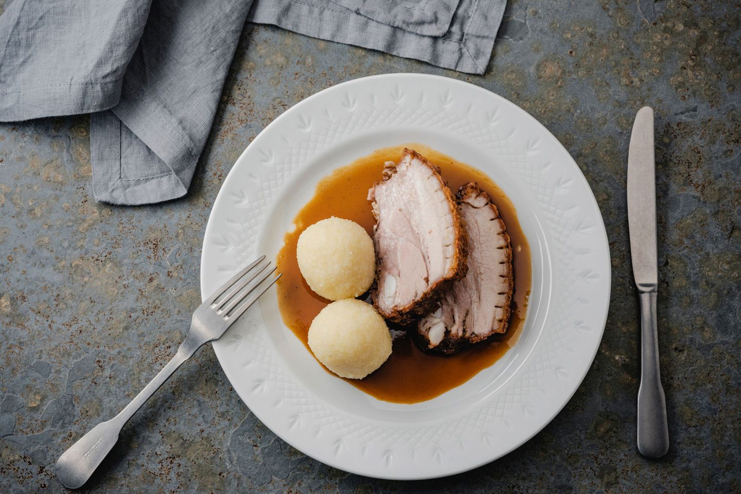 2 Scheiben Schweinsbraten mit Kartoffelknödeln und Sauce auf einem Teller mit Gabel