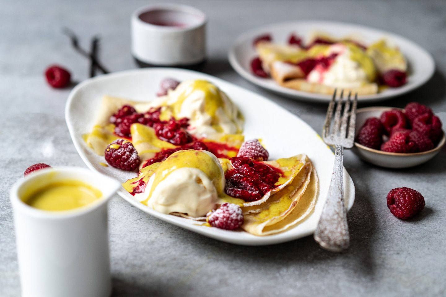 Palatschinken mit Golden Milk Sauce, Vanilleeis und heißen Himbeeren auf 2 Tellern angerichtet und mit Staubzucker bestreut