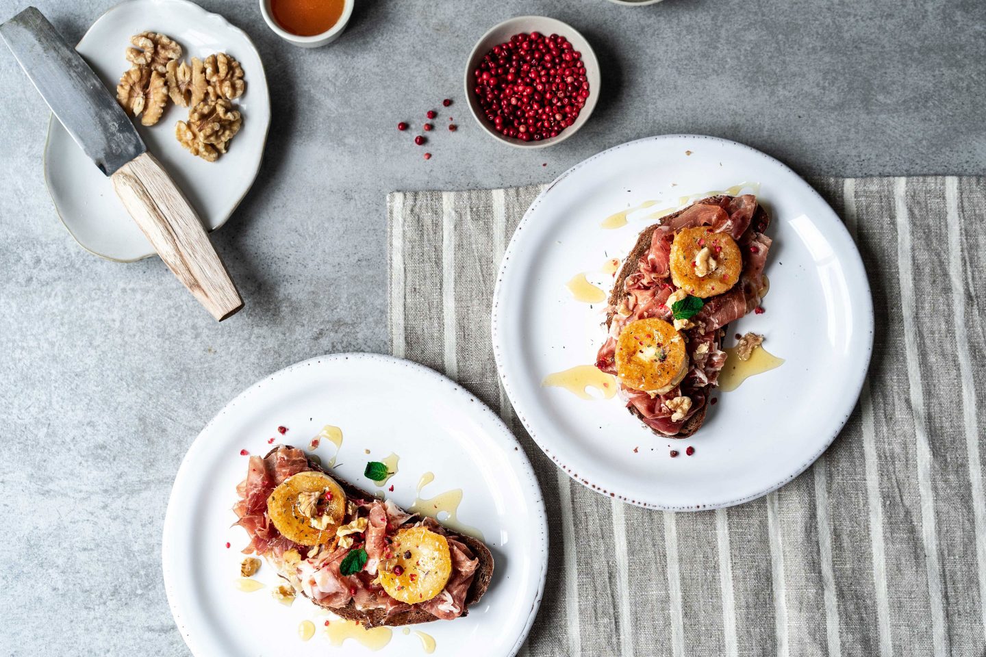 " Scheiben Schwarzbrot mit Ziegenkaese, iner schale mit Rosa Beeren und Walnüssen auf einer Steinplatte