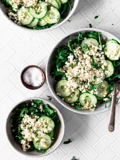 frischer Quinoa Salat mit Gurkenscheiben auf 3 Schüsseln verteilt auf einem gefliesten, weißen Untergrund