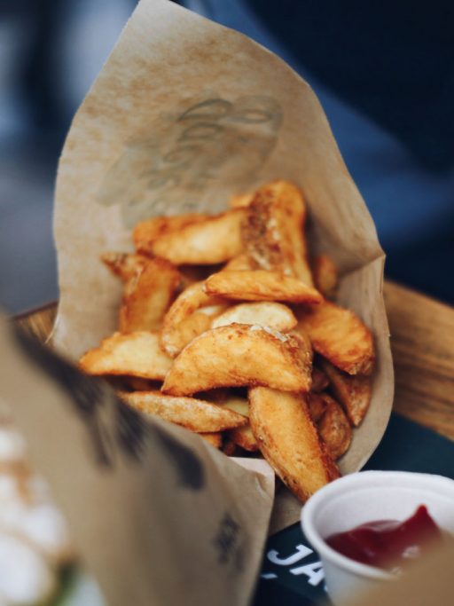 Ein Papiersackerl mit Wedges gefüllt, davor etwas Ketchup in einem Schälchen