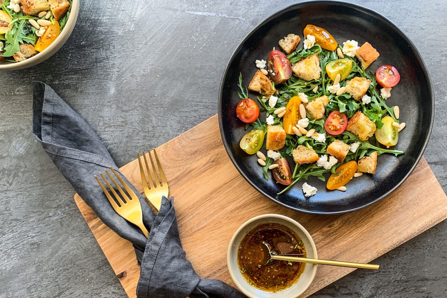 Mediterrander Brotsalat mit gelben und roten Cocktailtomaten und Rucola auf einem schwarzen Teller angerichtet