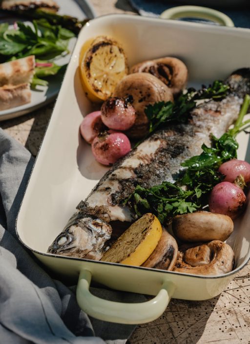 gegrillte Forelle in einer Emailleform mit gegrilltem Gemüse an einem gedeckten Tisch