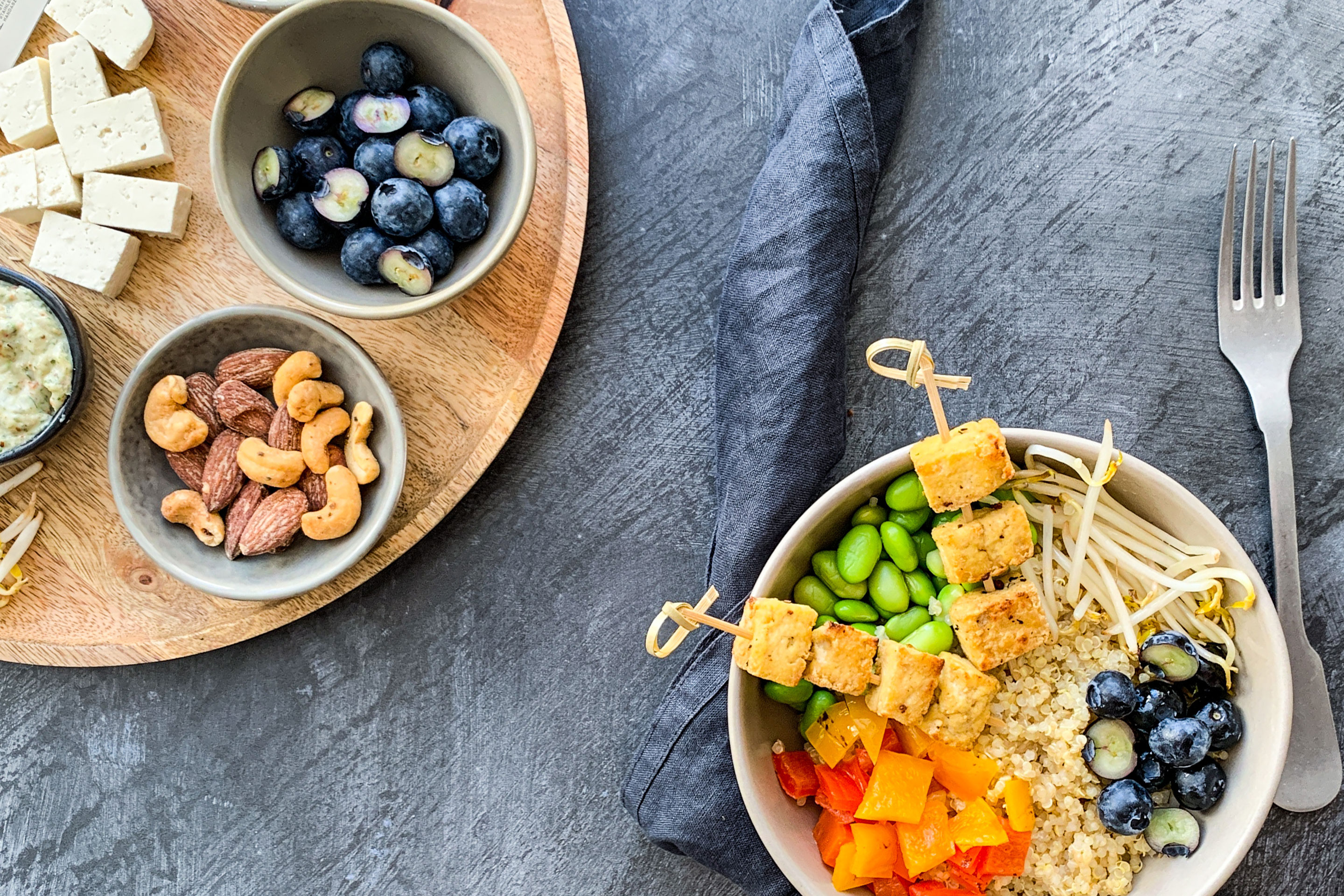 Quinoa-Bowl mit frittierten Tofu-Würfeln, Nüssen und Heidelbeeren in einer Schale angerichtet