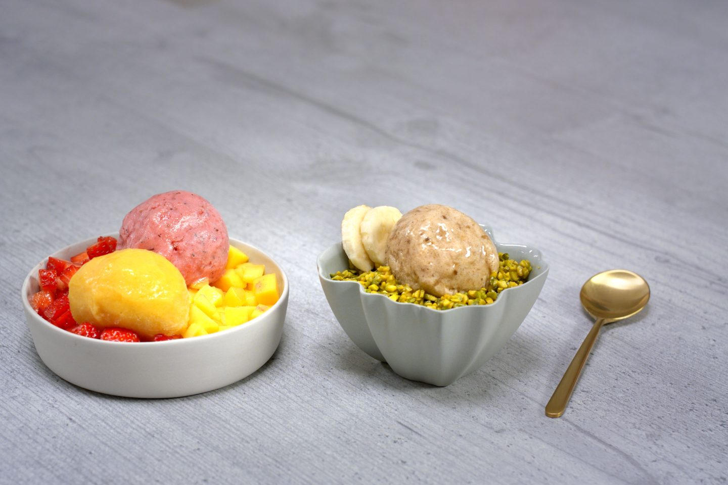 Frucht Eis mit Pistauen und frischen Früchten angerichtet in 2 Schälchen mit goldenem Löffel