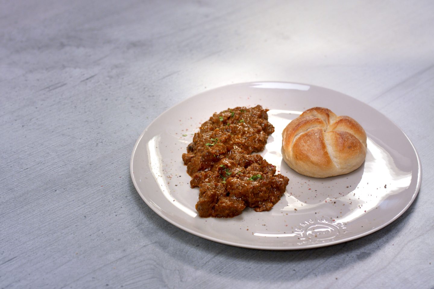 Schawarzbiergulasch mit einer Semmel auf einem gräulichen Teller