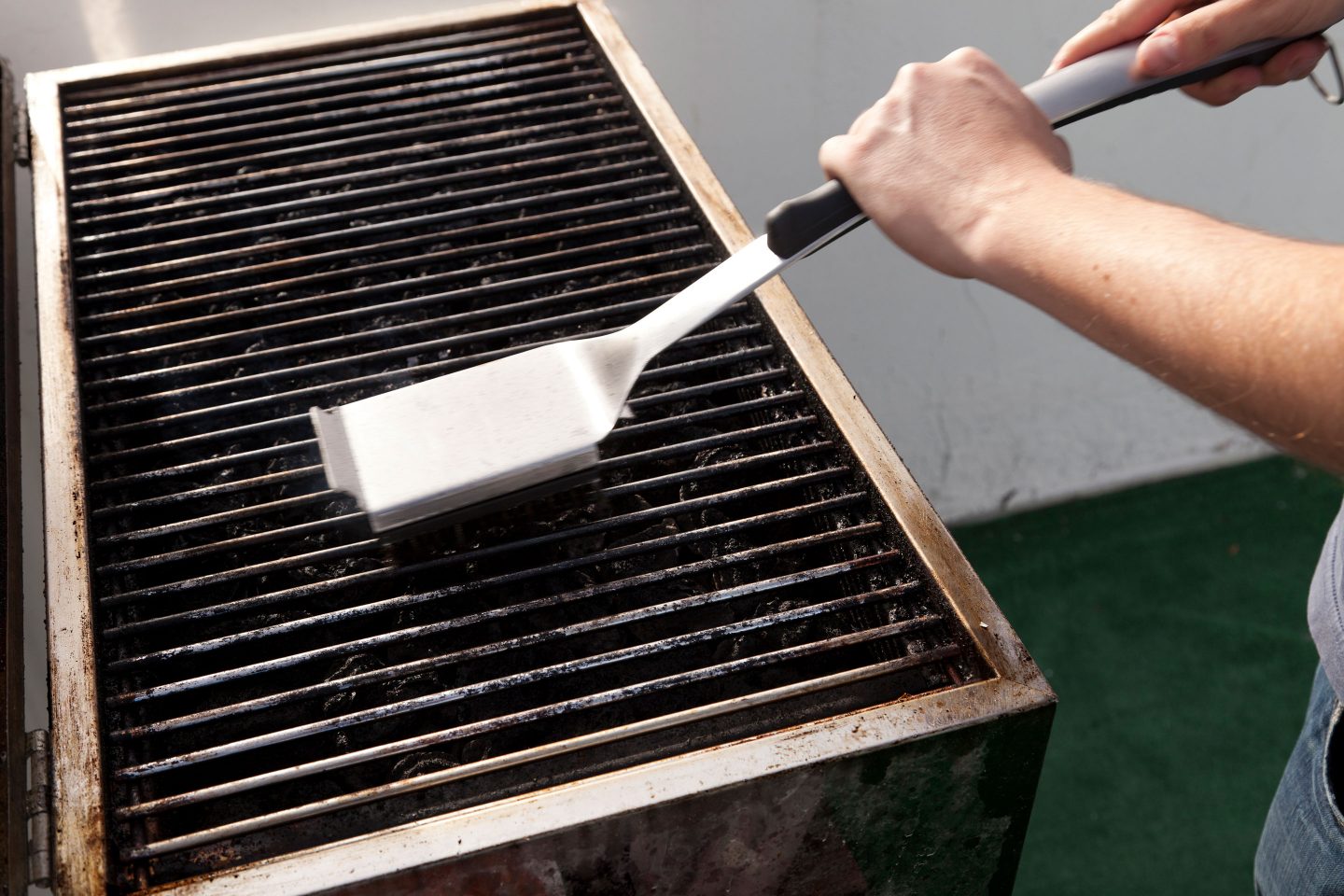 MAnn reinigt Griller mit einer Grillbürste
