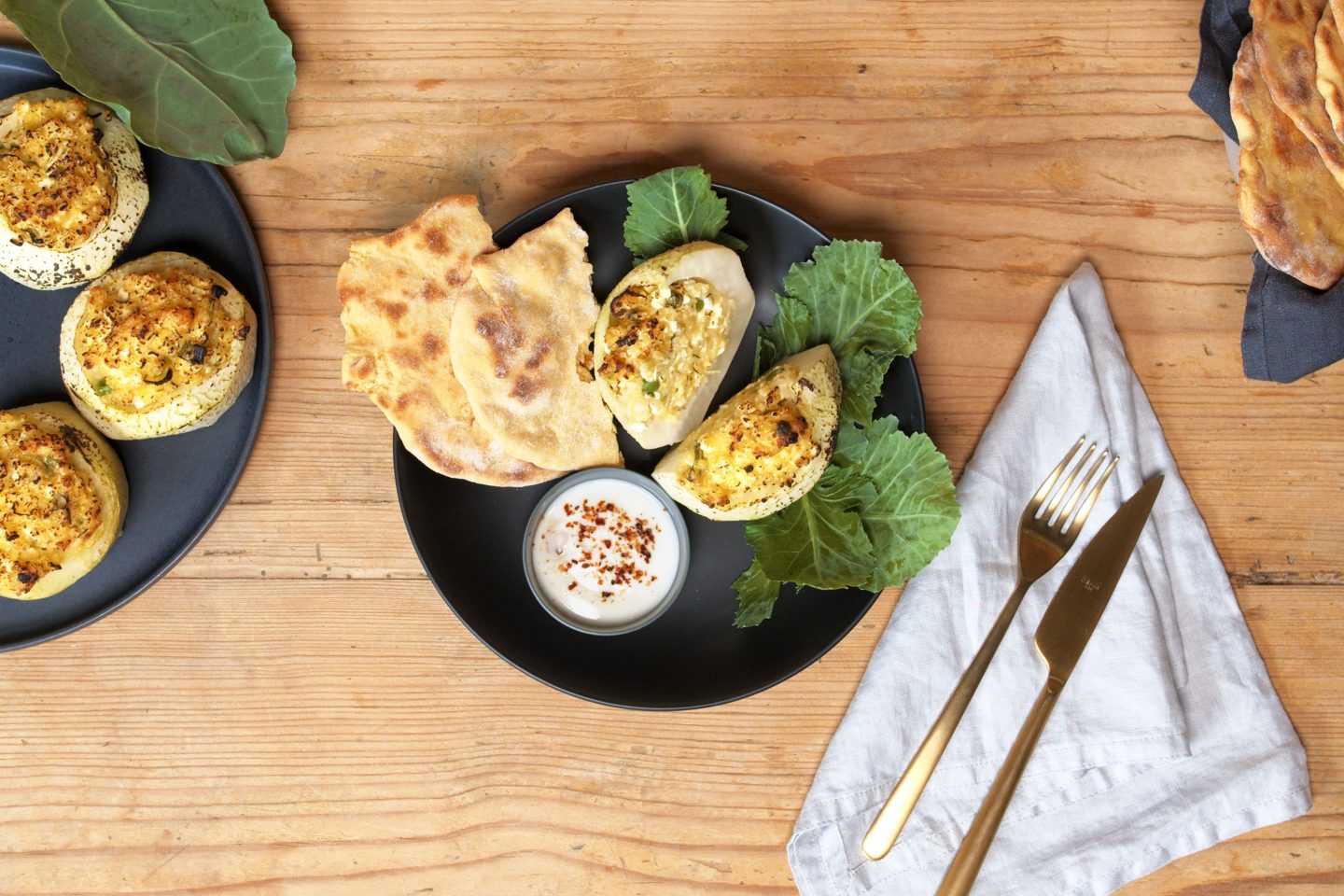 Gegrillte Kohlrabihälften auf einem schwarzen Teller mit selbst gemachtem Fladenbrot auf einem Holztisch
