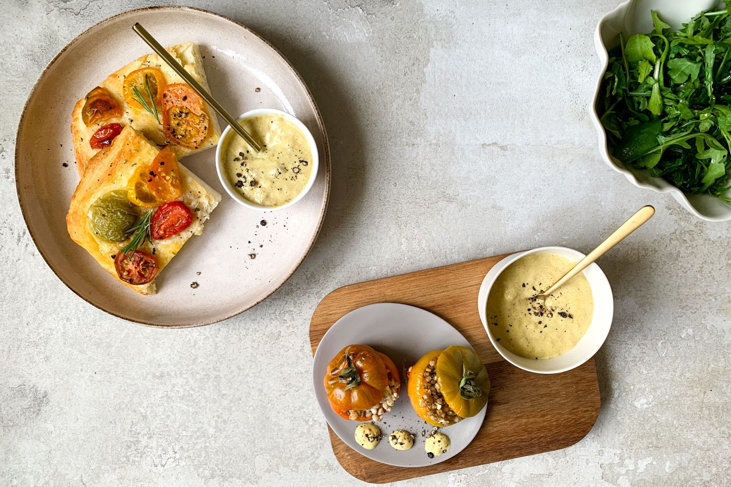 Gefüllte Tomaten auf einem Tellerchen, daneben ein Schälchen mit Curry-Bananen-Dip mit goldenem Löffel auf einem Holzbrett