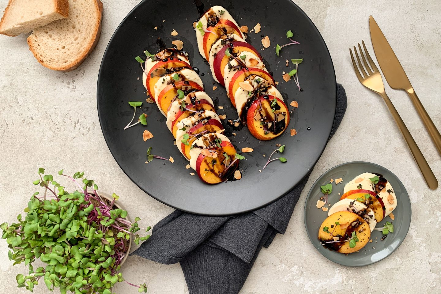 Caprese aus Mozzarella- und Nektarinenscheiben mit frischem Basilikum und Crema di Balsamico garniert auf einem schwarzen Teller