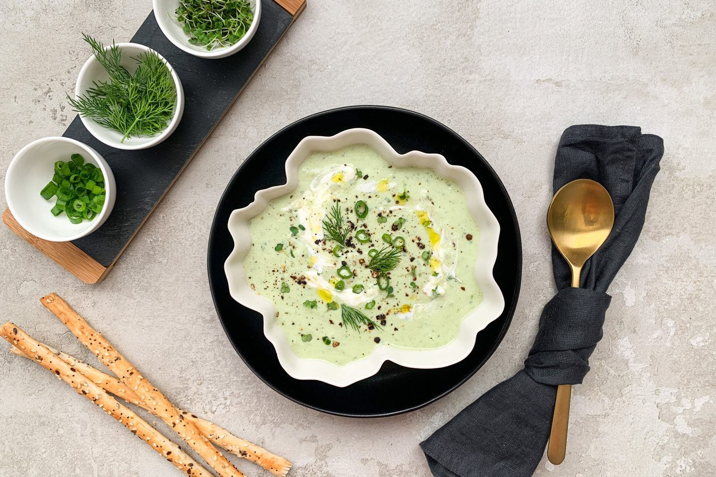 kalte Avocado-Gurken-Suppe in einer beigen schale mit Crissini und frischen Kräutern