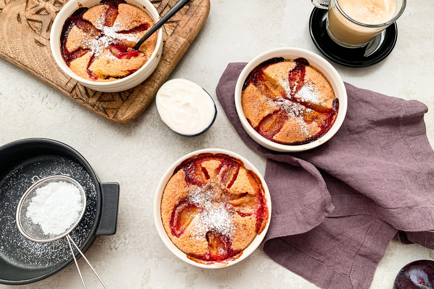 3 Schälchen mit Clafoutis dazu eine Tasse Cappuccino und Staubzucker