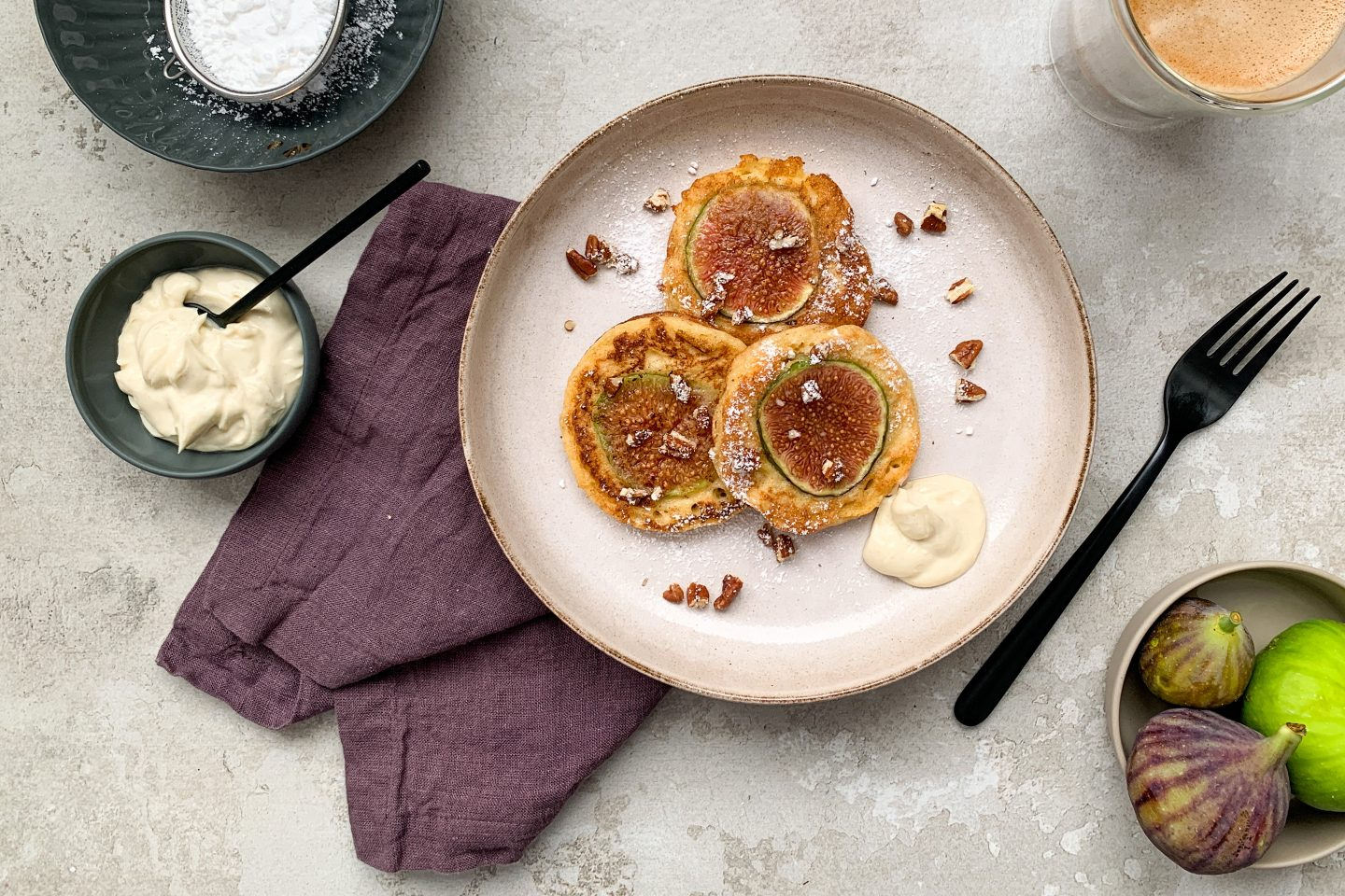 Feigen Pancakes auf einem rustikalen Teller mit Staubzucker, Cardamomcreme und frischen Feigen