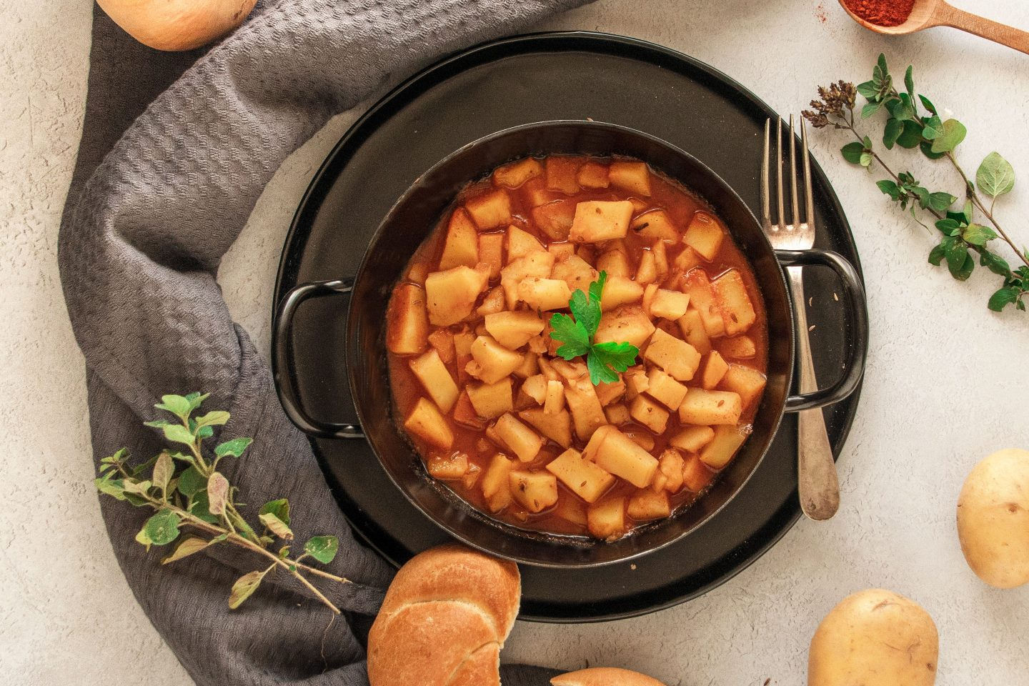 Kartoffelgulasch in einem schwarzen Reindl mit Gabel und Semmel auf einem dunklen Teller