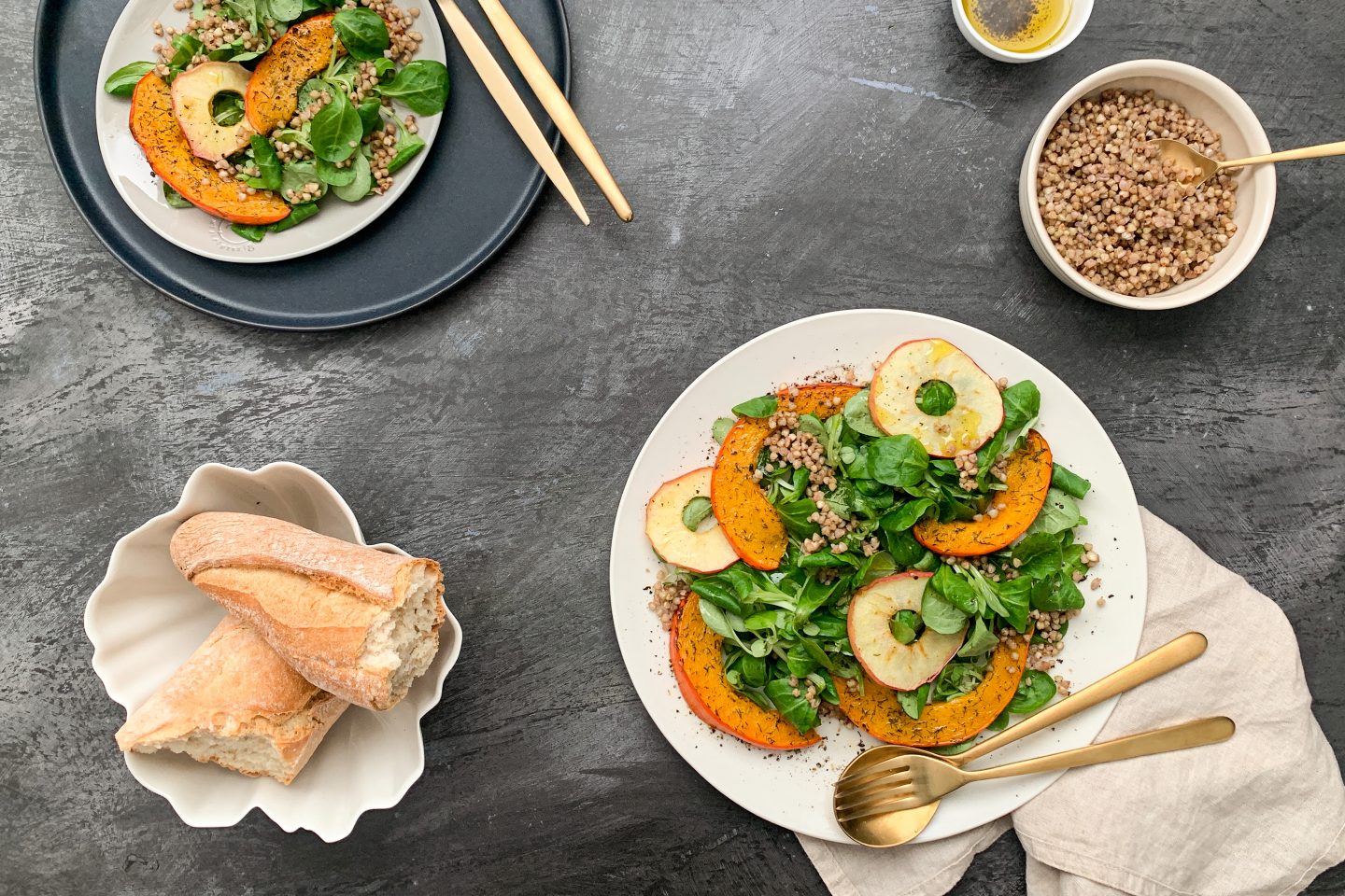 Kürbis-Apfelsalat mit knusprigen Buchweizen auf 2 Tellern angerichtet mit Baguette und goldenem Besteck