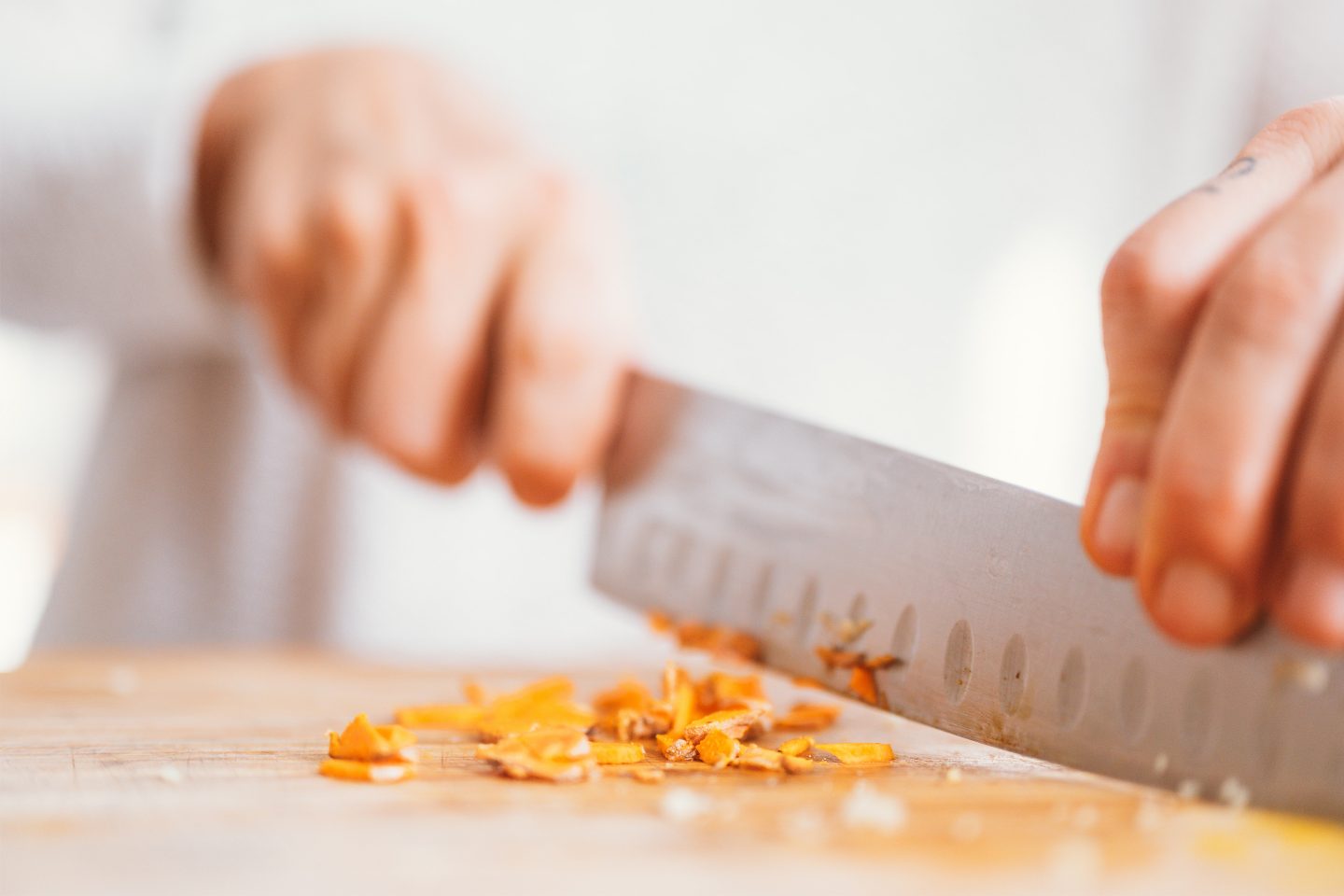 Frauenhand schneidet Curcumawurzel mit einem großen scharfen Messer