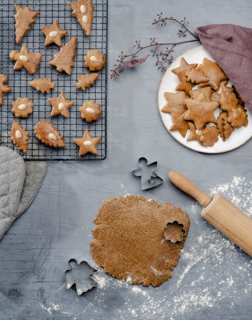 Gebackene Lebkuchen auf einem Kuchengitter und hellem Teller; ausgerollter Lebkuchenteig mit Ausstechern