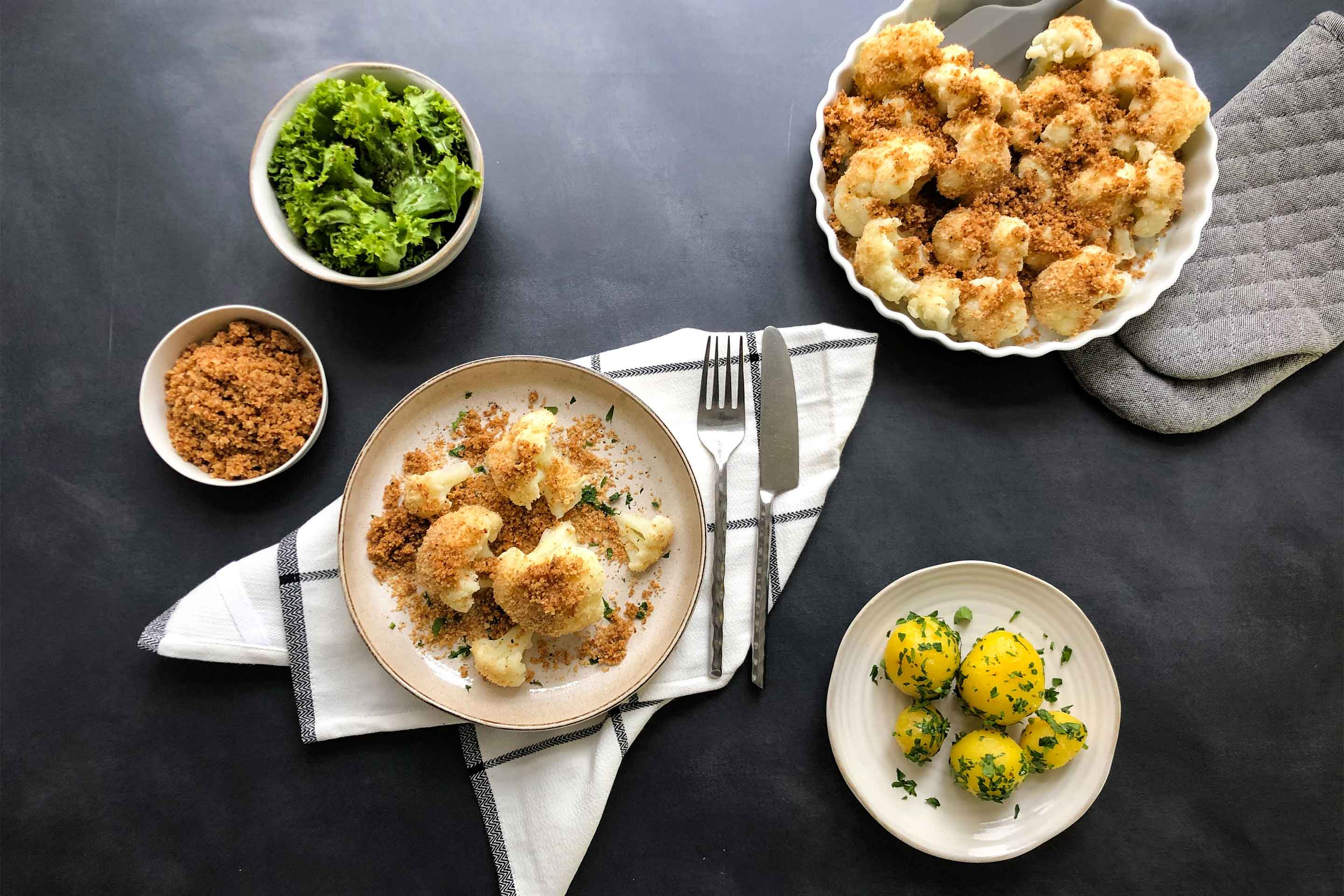 Karfiol Mit Butterbroesel auf einem rustikalen Teller mit grünem Salat und Petersilerdaepfeln als Beilage