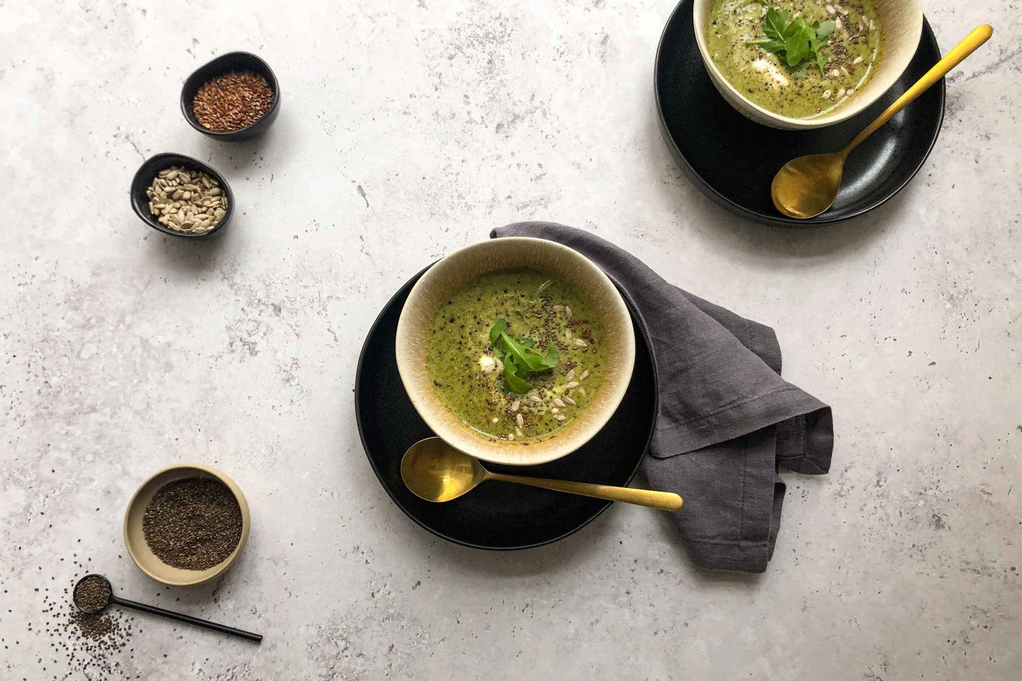 2 Schalen voller Brokkoli-Detox-Suppe auf dunklen Tellern mir goldenen Löffeln
