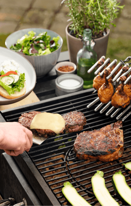 Burger Pattys, Hühnerkeulen auf Deckelhalter und Kotelette auf dem Grill.
